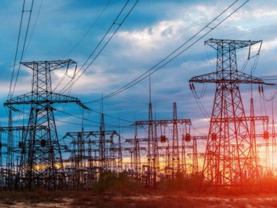 Power lines and transmission towers against a blue and orange sky at sunset.