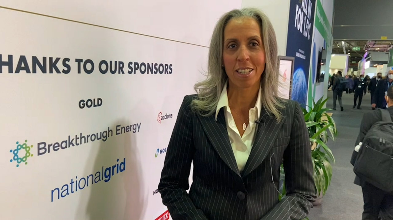 Person standing in front of a sponsor wall at an event, wearing a pinstripe suit.