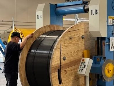 A worker operates a large machine with a wooden spool in an industrial setting.