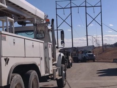 Utility trucks parked on a paved road beneath a large metal structure under a clear sky.