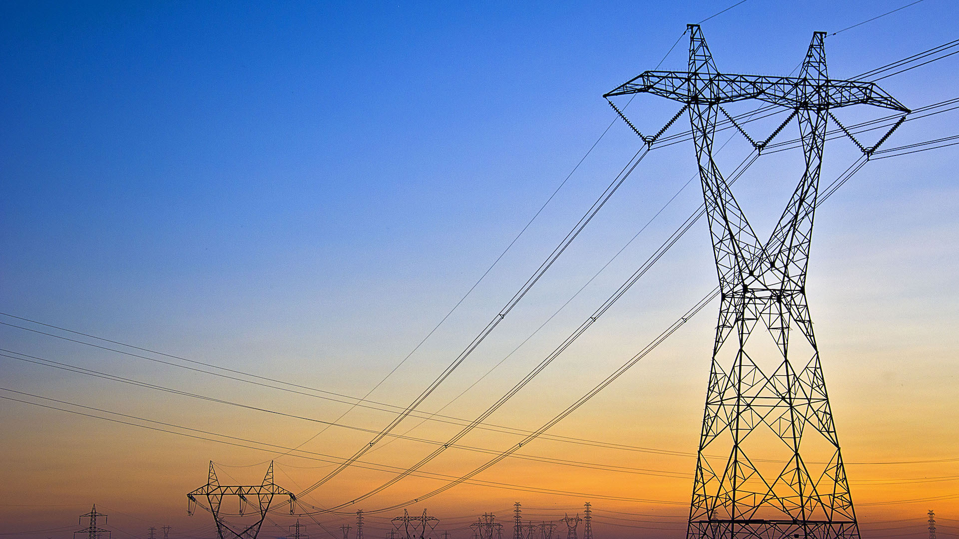 Tall power lines against a sunset sky with a gradient of blue to orange.