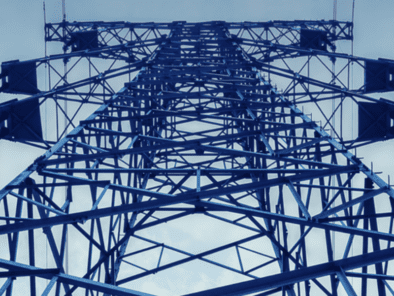 Upward view of a blue metal transmission tower against a cloudy sky.