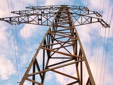 Upward view of an electricity transmission tower against a partly cloudy sky.