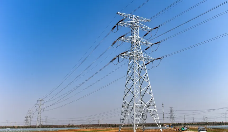 High-voltage transmission tower with power lines against a clear blue sky in an open area.