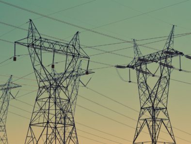 Two large electricity pylons with interconnected power lines set against a gradient sky during dusk.