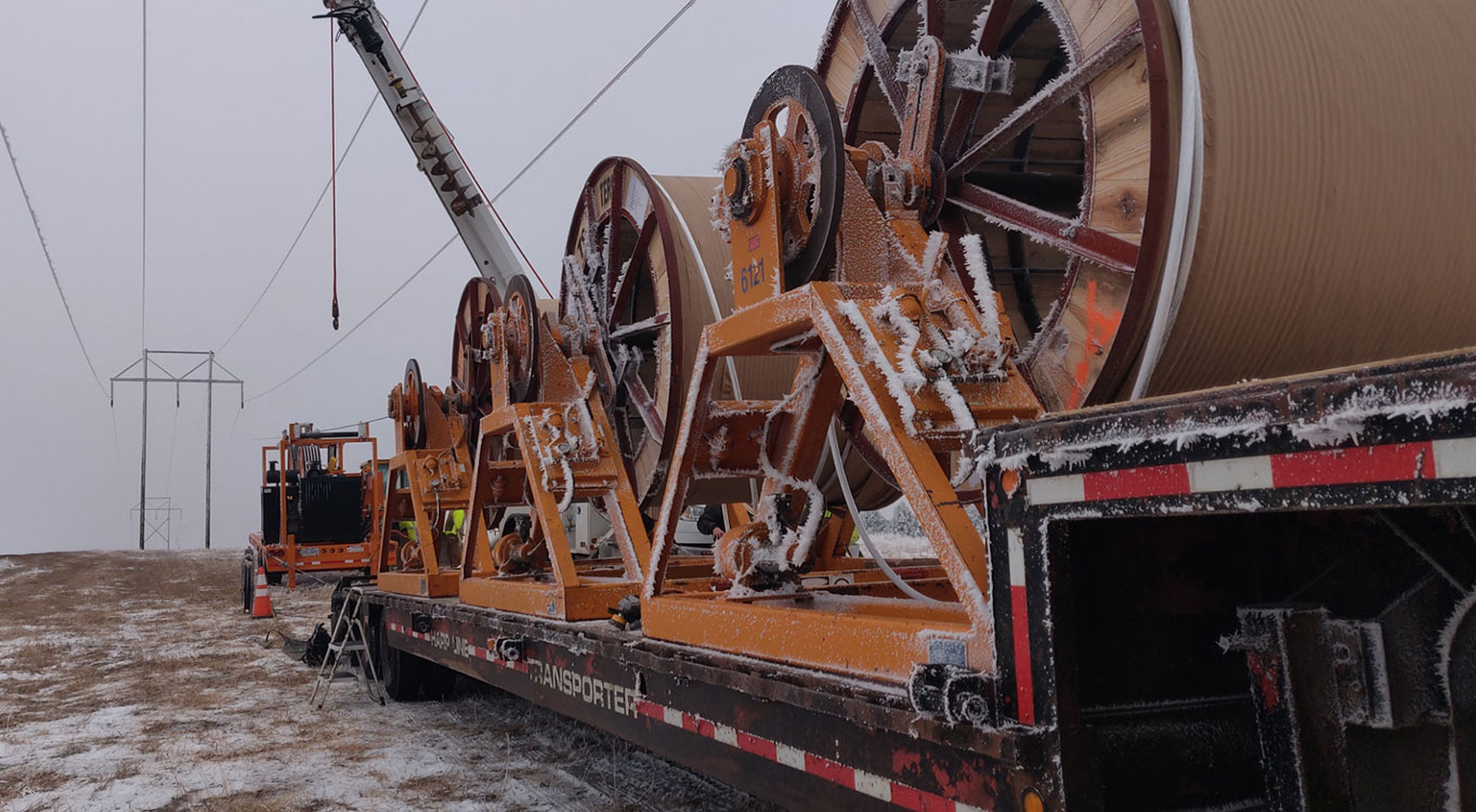 Large spools of cable on an orange reel trailer in a snowy landscape, used for power line installation.