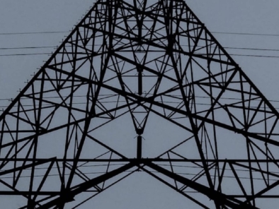 View of a tall metal electricity pylon against a gray sky, showcasing the intricate lattice structure and multiple power lines.