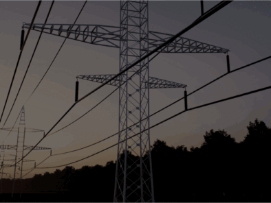 High-voltage power lines and transmission towers stretch across a landscape at sunset, with trees silhouetted in the background.
